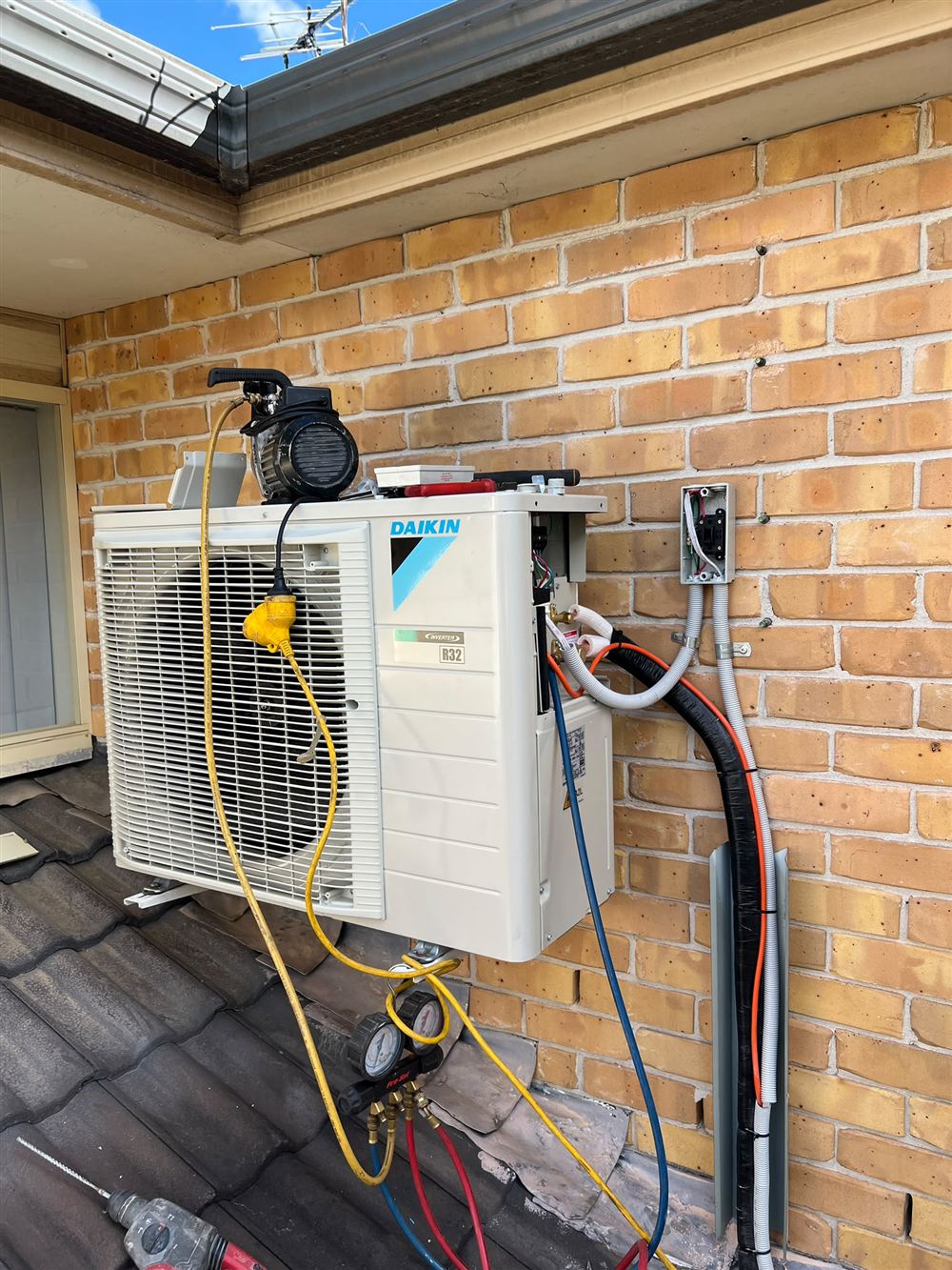 Outdoor air conditioning unit being commissioned on a brick wall with gauges and vacuum pump connected
