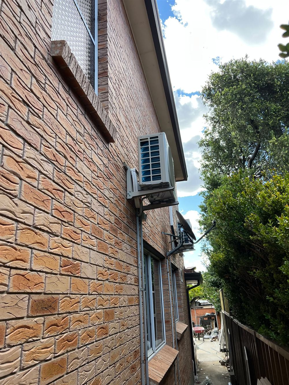 Outdoor air conditioning units mounted on wall brackets on a two-storey brick house