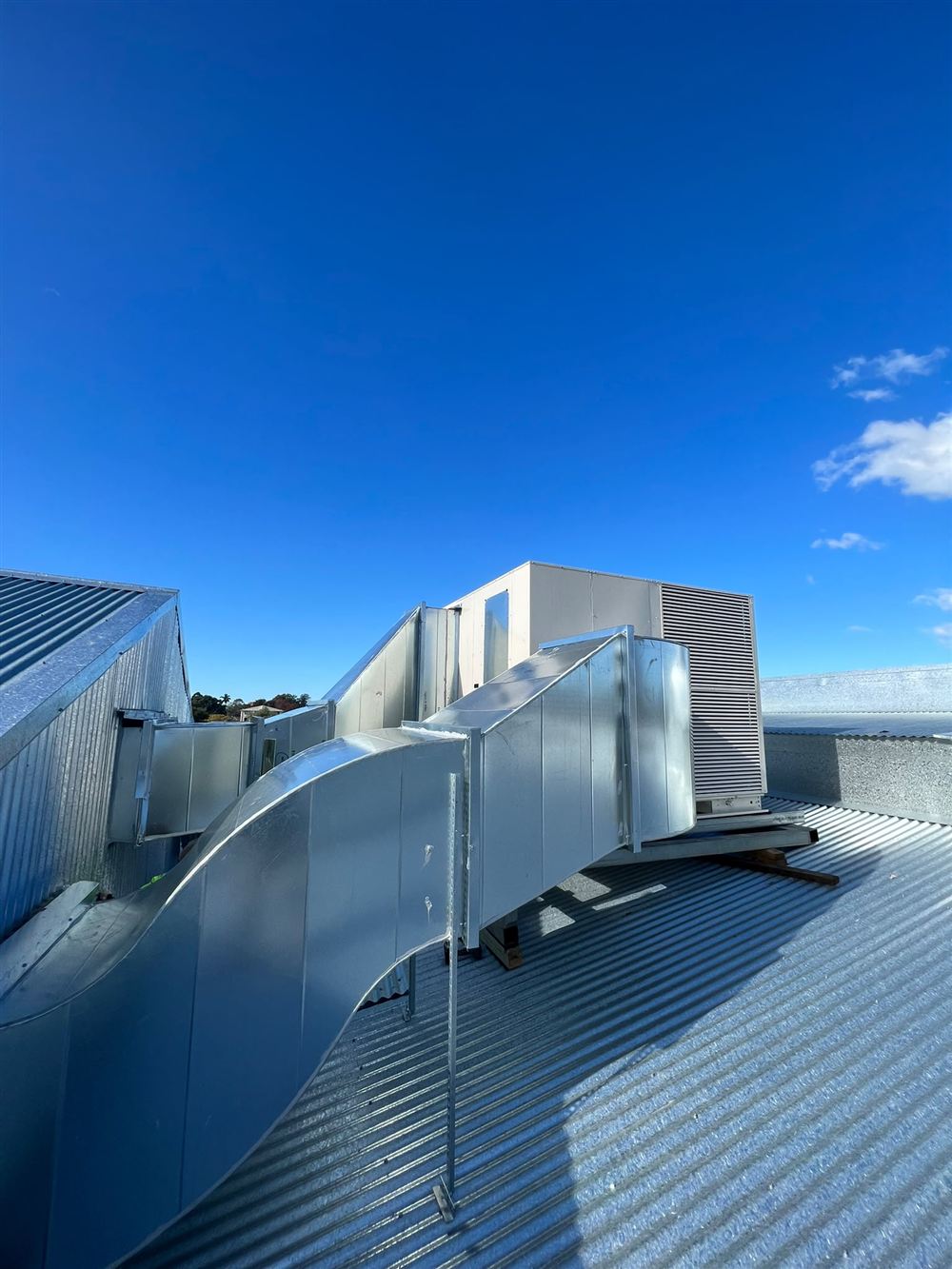 Galvanised steel HVAC ductwork connected to a rooftop unit on a commercial building